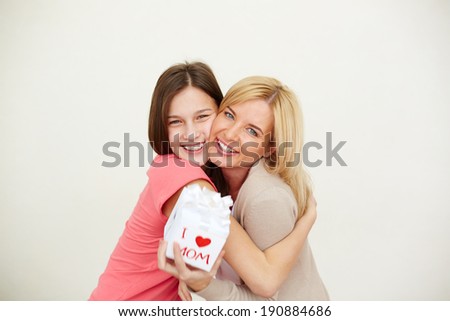 Teenage girl and her mom with small present looking at camera and laughing