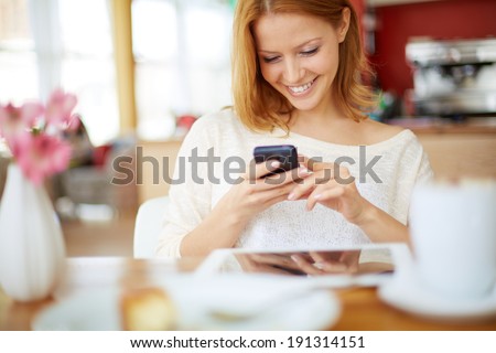 Image of young female reading sms on the phone in cafe Image of young female reading sms on the phone in cafe