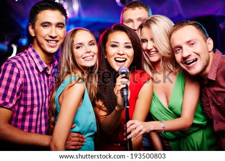 Portrait of happy girls and guys singing in microphone in the karaoke bar