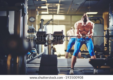 Portrait of sporty topless man lifting weight in gym
