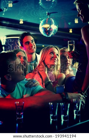 Portrait of cheerful girls and guys with cocktails looking at their friend in the bar