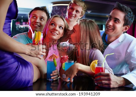 Portrait of cheerful girls and guys with cocktails looking at their friend in the bar