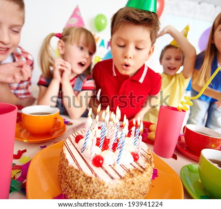 Group of adorable kids looking at birthday cake with candles, cute boy blowing on them