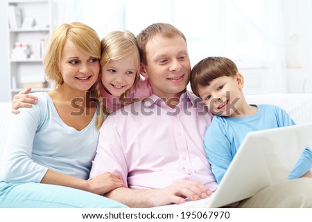 A young family of four sitting on sofa and looking at laptop screen