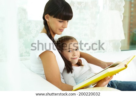 Portrait of cute girl and her mother reading a book at home