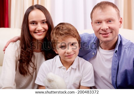 Portrait of happy family of three looking at camera at home