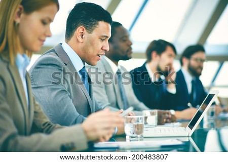 Row of business people listening to presentation at seminar with focus on elegant young man