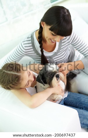 Cute girl holding pet and looking at it with her mother near by