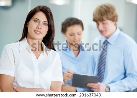 Portrait of beautiful secretary in white shirt looking at camera on the background of co-workers