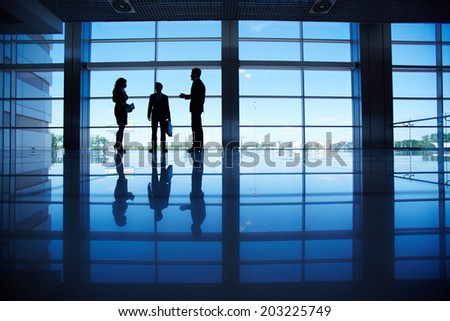 Silhouettes of several office workers standing by the window and talking