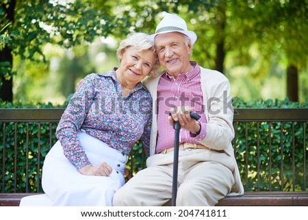 Happy seniors sitting on bench in the park and looking at camera