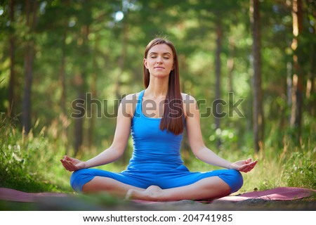 Portrait of calm woman sitting in pose of lotus in natural environment