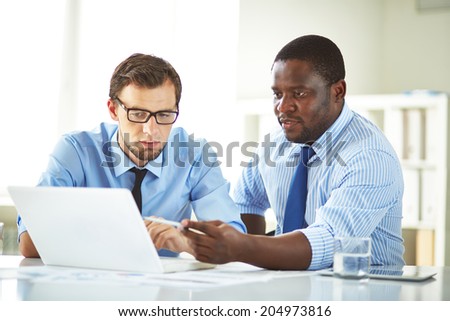 Image of two young businessmen using laptop and interacting at meeting Image of two young businessmen using laptop and interacting at meeting