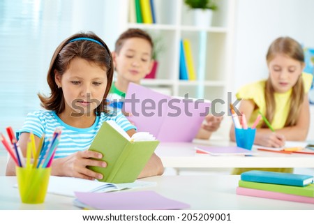 Portrait of serious girl with notepad reading notes on background of her classmates