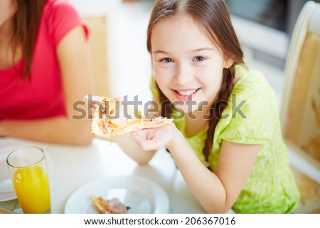 Portrait of cute little girl sitting by dinner table and eating pizza