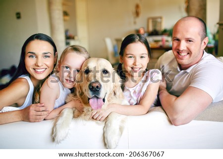 A young friendly family of four with pet looking at camera at home