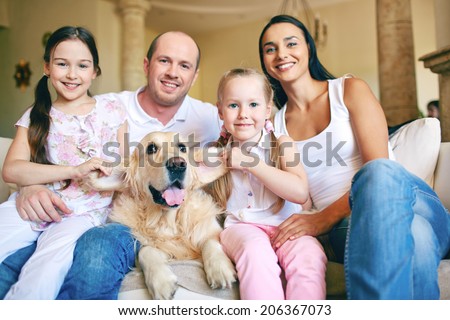 Modern family of father, mother, two daughters and dog posing for camera at home