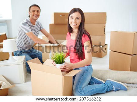Happy young couple sitting on the floor of new flat and unpacking boxes