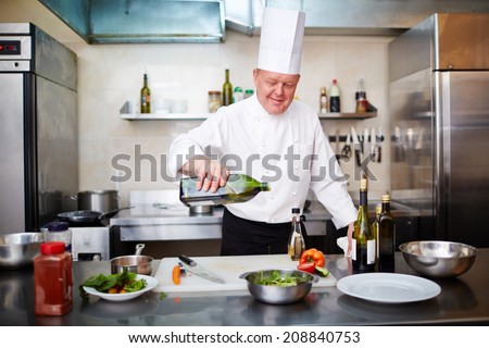 Image of male chef pouring olive oil into vegetable salad in the kitchen
