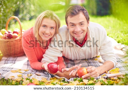 Happy young couple with ripe apples relaxing on lawn in park