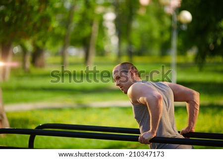 Young man having physical training on sport equipment outside
