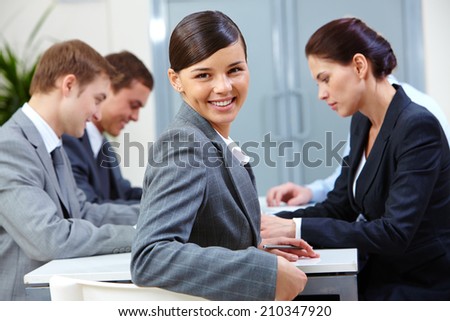 Portrait of beautiful secretary looking at camera on the background of co-workers