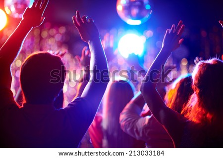 Crowd of people with raised arms dancing in night club