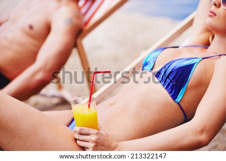 Woman with juice resting in deck chair with man on background