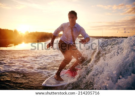 Young man in wet clothes surfboarding at summer resort