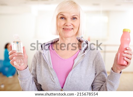 Happy mature woman with plastic bottles of water and yoghurt looking at camera
