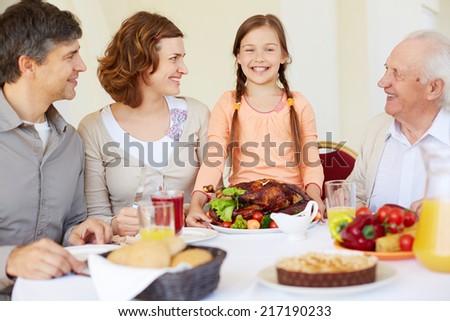 Portrait of happy family looking at joyful girl during Thanksgiving dinner