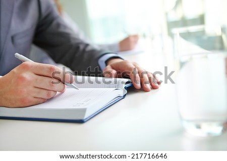 Hand of businessman with pen writing in notebook at seminar