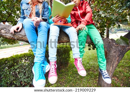 Casual schoolkids sitting on tree branch and reading