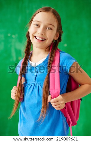 Cheerful child with backpack looking at camera in isolation