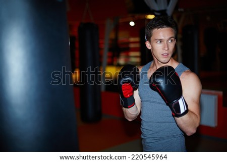 Portrait of young man in boxing gloves in sports gym