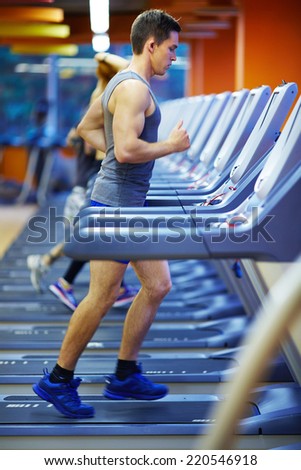 Attractive man running on special sport equipment in gym