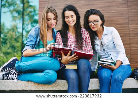 Company of happy teen girls reading book outside
