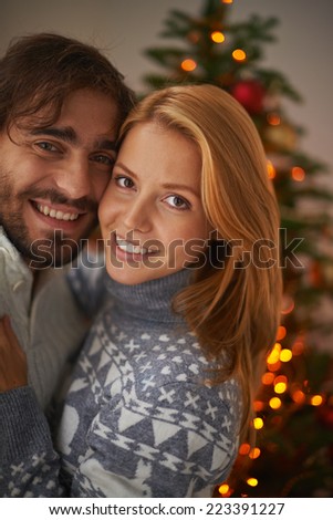 Affectionate couple looking at camera on xmas evening with sparkling firtree on background