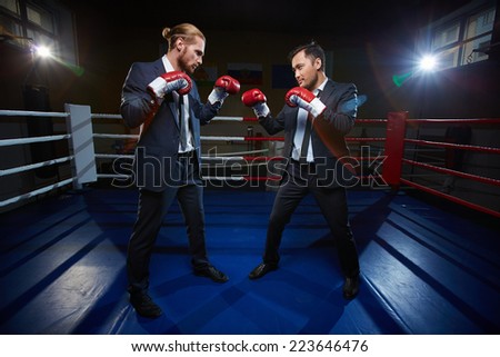 Professional businessmen in suits and boxing gloves standing opposite one another on boxing ring