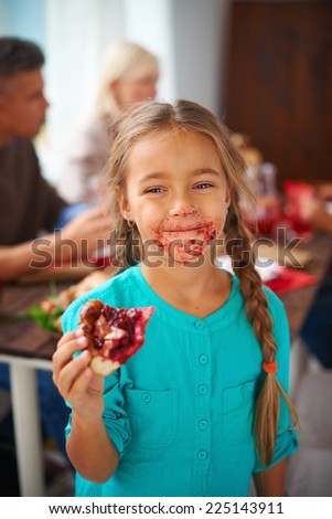 Portrait of smudgy girl eating sweet pie on background of her parents
