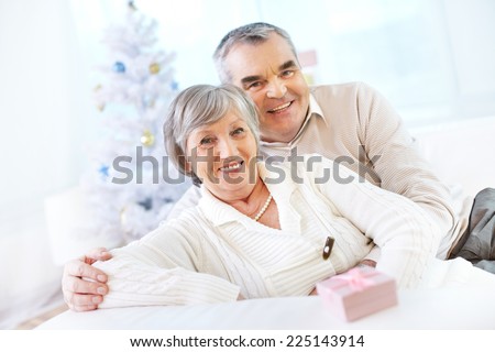 Happy seniors looking at camera and smiling on background of Christmas tree
