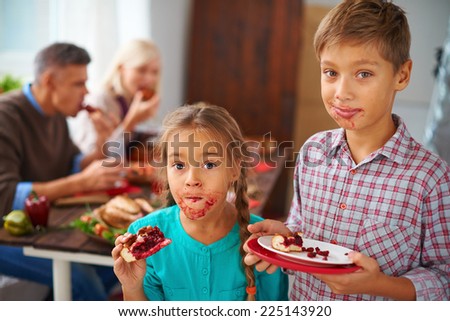 Portrait of funny kids eating sweet pie on background of their parents