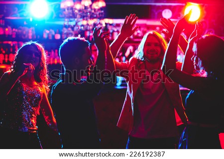 Ecstatic friends with raised arms dancing in nightclub