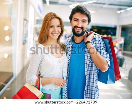 Portrait of young couple with paperbags looking at camera after shopping