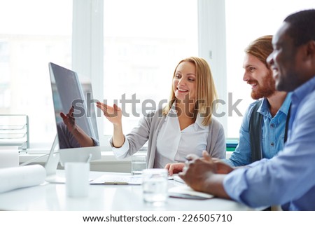 Male employees looking at computer monitor while their female colleague presenting new project