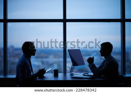 Outlines of two businessmen working late in office