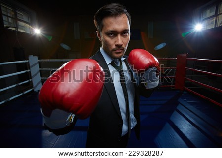 Serious businessman in suit and boxing gloves looking at camera