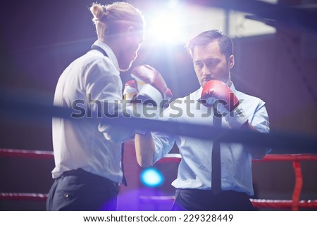 Elegant businessman in formalwear and boxing gloves looking at his rival before attack