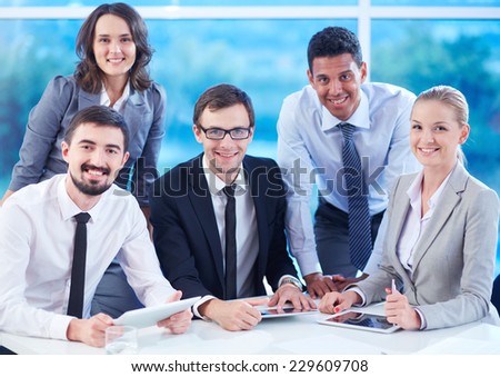 Group of smiling colleagues with touchpads looking at camera in office