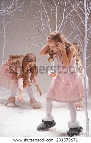 Playful girls in smart dresses playing snowballs in winter forest